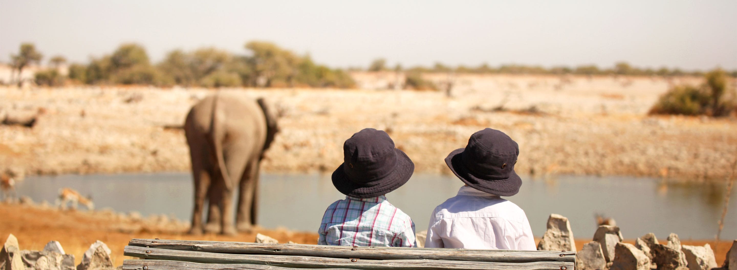 Two young kids watching an elephant at a watering hole