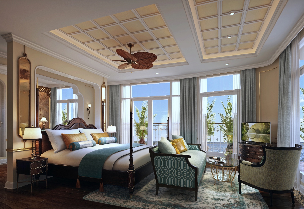 A luxurious cruise ship suite bedroom featuring a dark wood four-poster bed with white linens and a teal accent throw. The room has an elegant coffered ceiling with warm lighting and a ceiling fan. Large floor-to-ceiling windows and glass doors open to a private balcony with palm trees visible outside, suggesting a tropical location. The suite includes a sophisticated seating area with a teal patterned bench and olive green armchair, a dark wood entertainment center with TV, and warm beige walls with classic molding.