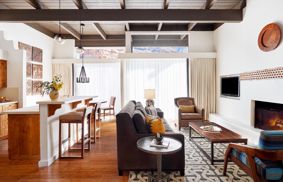 Soaring wood beam ceilings and clerestory windows frame breathtaking glimpses of Sedona's iconic red rock formations in this light-filled Southwest sanctuary, where an open-concept living space flows seamlessly from kitchen bar to dining area to fireside lounge. Rich walnut floors anchor the contemporary desert aesthetic, complemented by charcoal linen sofas accented with golden pillows, sculptural Native American art, and leather furnishings that create an inviting retreat infused with both modern sophistication and regional soul.
