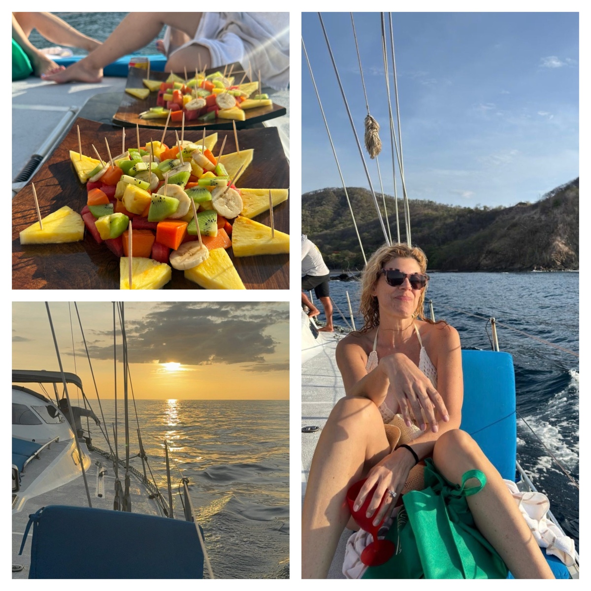 A woman in sunglasses reclines against a blue cushion on the deck of a moving sailboat, holding a red drinking glass. The boat's wake trails across dark blue water beside a dry, scrub-covered coastal hillside under a clear sky.